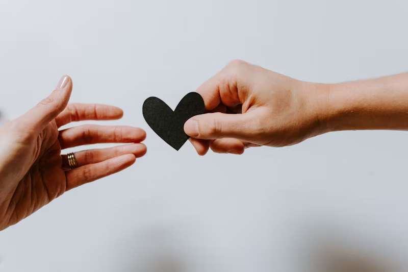 A black heart being passed between two hands representing the caring nature of Allied Trades mental health rehab.